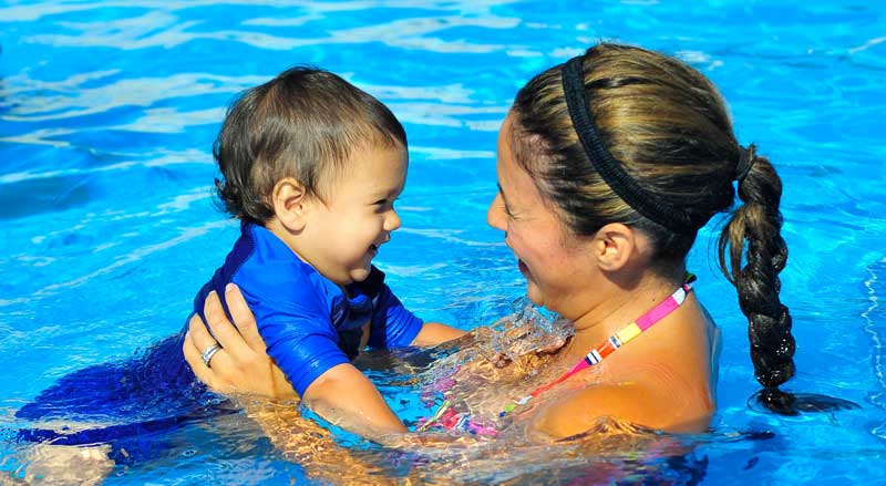 A young toddler being held by an adult in a pool