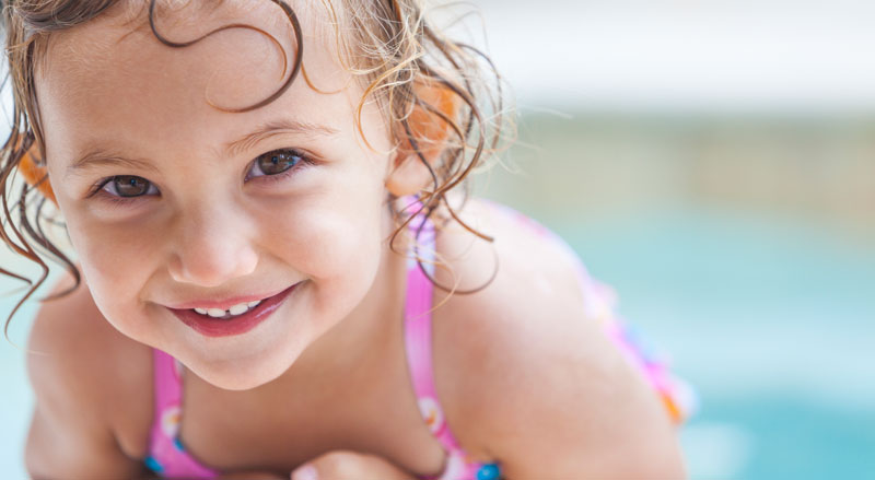 A young girl in a pool smiles at the camera