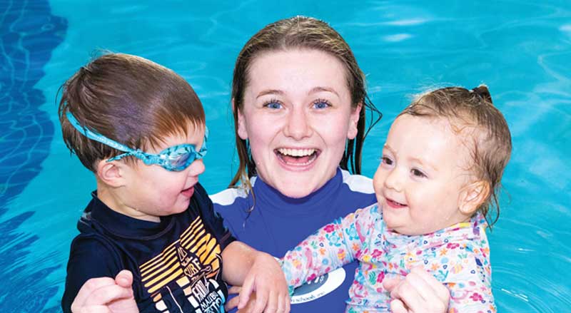 Njswim teacher holding two happy toddlers during swim lesson