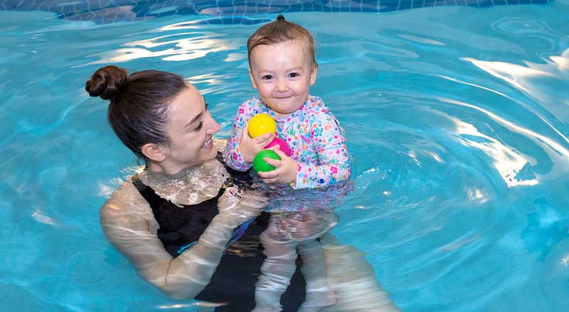 A toddler taking a swim lesson in a pool with her teacher