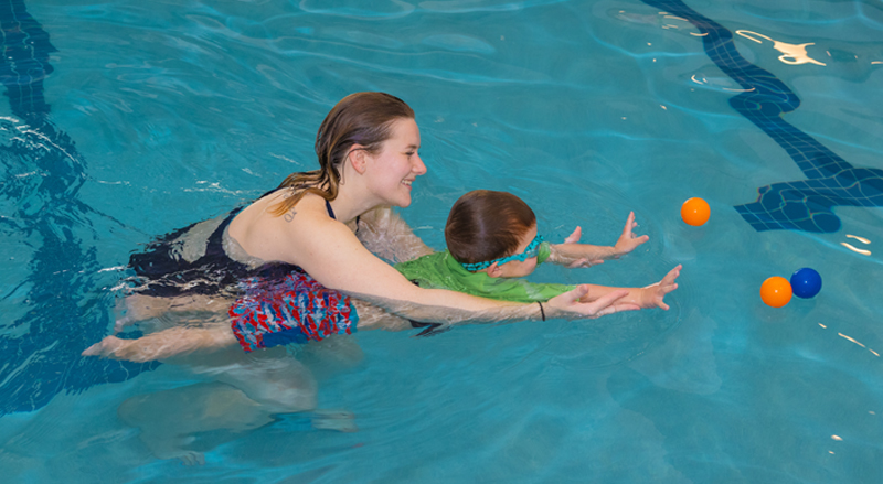 A young toddler in a pool is supported by an adult