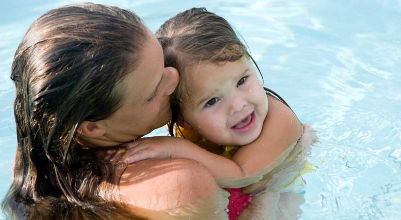 A toddler learning water safety in a pool with her mother