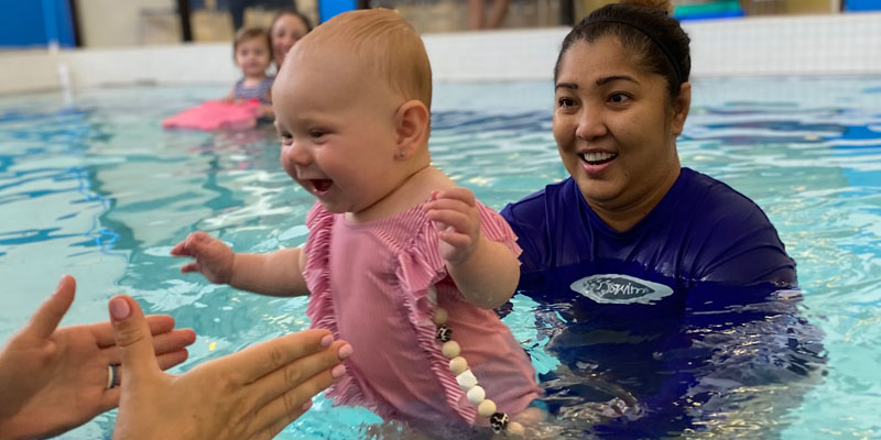 Smiling baby in a pool with parent and swim teacher