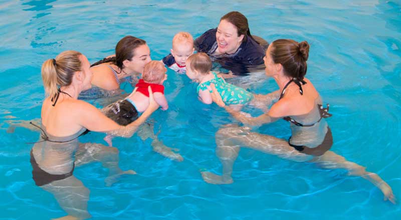 Babies, mothers, and instructor in pool enjoy a Water Babies class