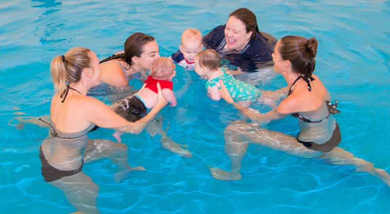 Three parents with their babies and a swim teacher in a Water Babies class
