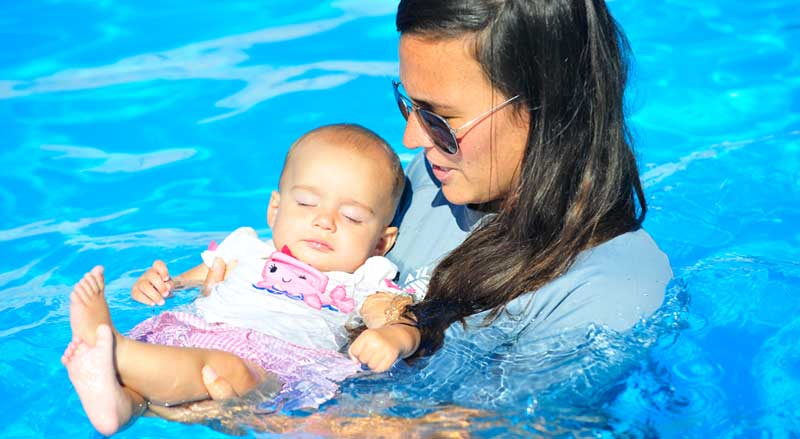 A young baby girl is supported by woman in pool