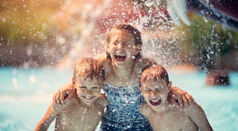 Three kids being splashed by water in a water park pool