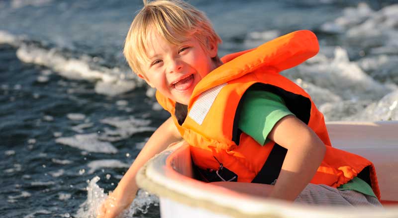 Kid wearing an orange life jacket in a boat on a lake