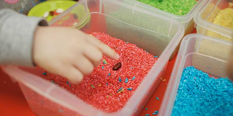 homemade-sensory-bin, pink sensory bin with child hand reaching in rice